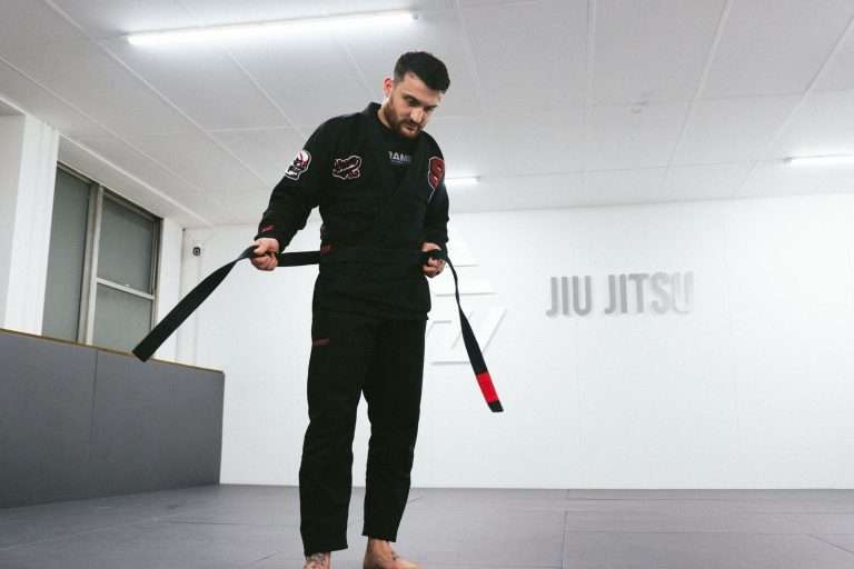 Man in a black Scramble BJJ Gi ties his black belt