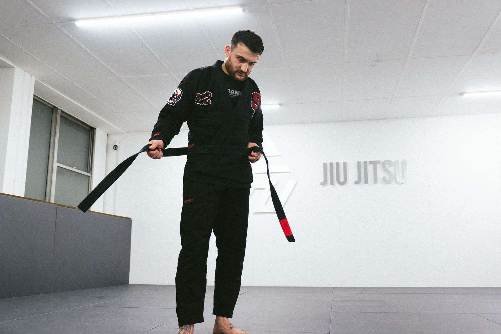Man in a black Scramble BJJ Gi ties his black belt